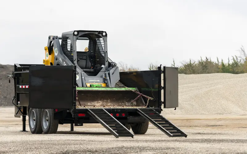 HD Low-Pro Dump Trailer with open loading ramps carrying a John Deere skid loader