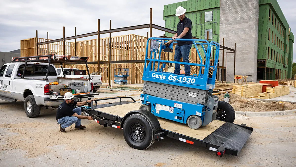 Two workers loading a scissor lift onto the Single Axle HD Tilt Trailer