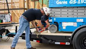 Two workers securing a scissor lift to the Single Axle HD Tilt Trailer