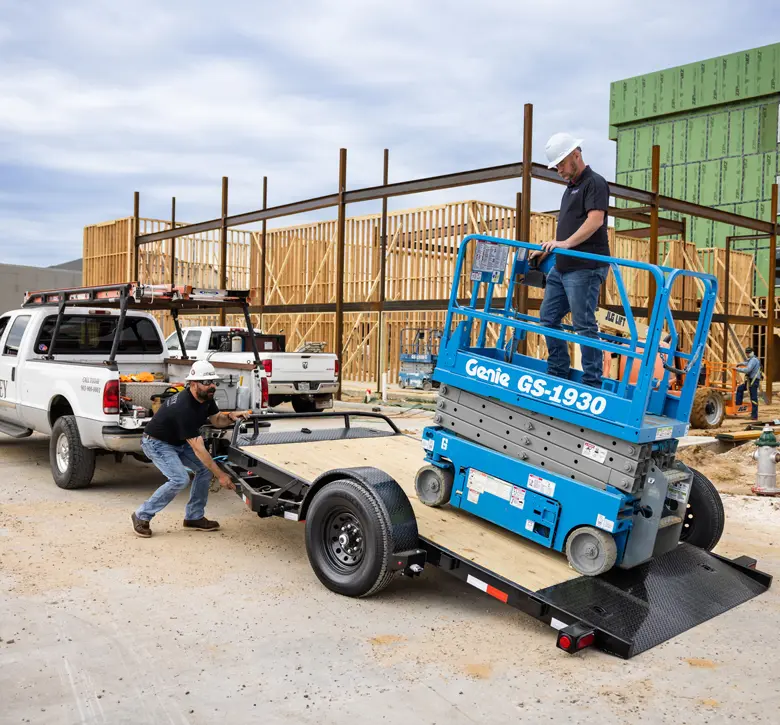 two males maneuvering a trailer and lift on the back of a pickup truck