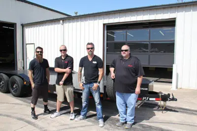 Four stars of the Fast N' Loud TV show standing with a trailer from PJ Trailers