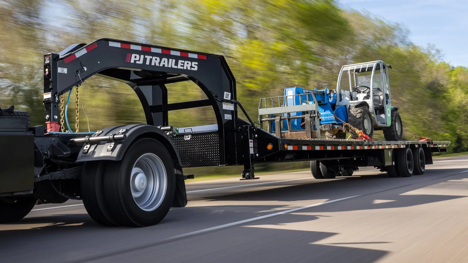 pj gooseneck deckover trailer driving on road hauling machinery