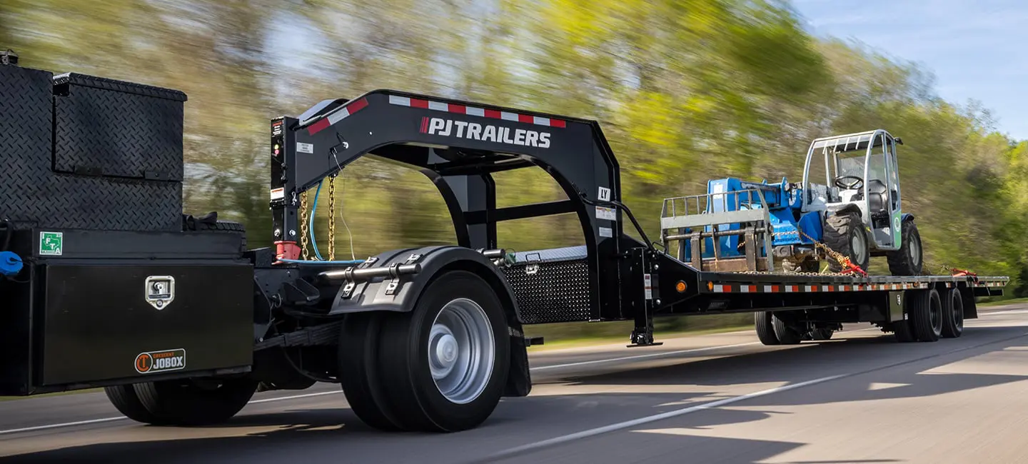 pj gooseneck deckover trailer driving on road hauling machinery