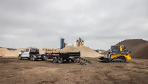 The Voyager Dump Trailer (DV) with lowered ramps preparing to carry a John Deere skid steer loader