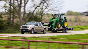 Truck carrying a John Deere front loader on the Low-Pro Flatdeck Trailer With 7K Singles