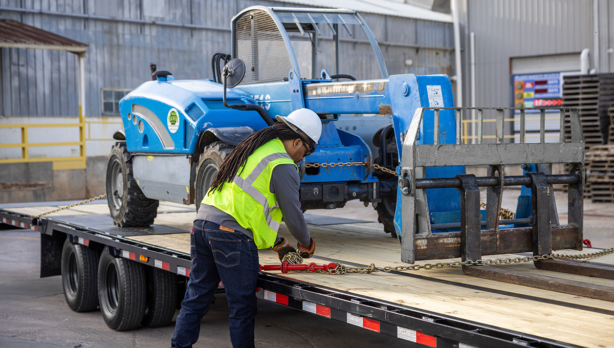 Worker strapping a forklift onto the Low-Pro With Hydraulic Dove Trailer