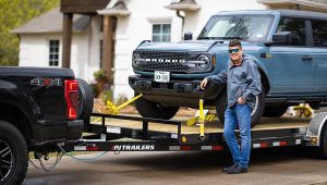 male standing in front of a trailer hooked to a pickup truck hauling a ford bronco