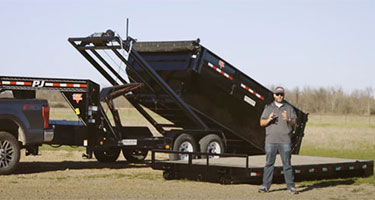 man standing in front of black truck and dump trailer